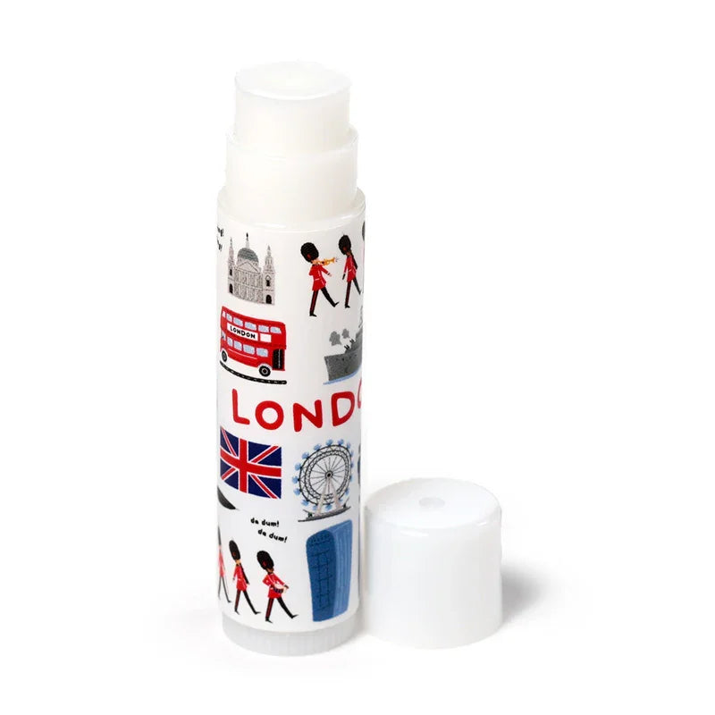Angled view of a white cylindrical London souvenir lip balm stick, featuring illustrations of a red double-decker bus, Union Jack flag, and London Eye. Its cap is removed and placed beside it.