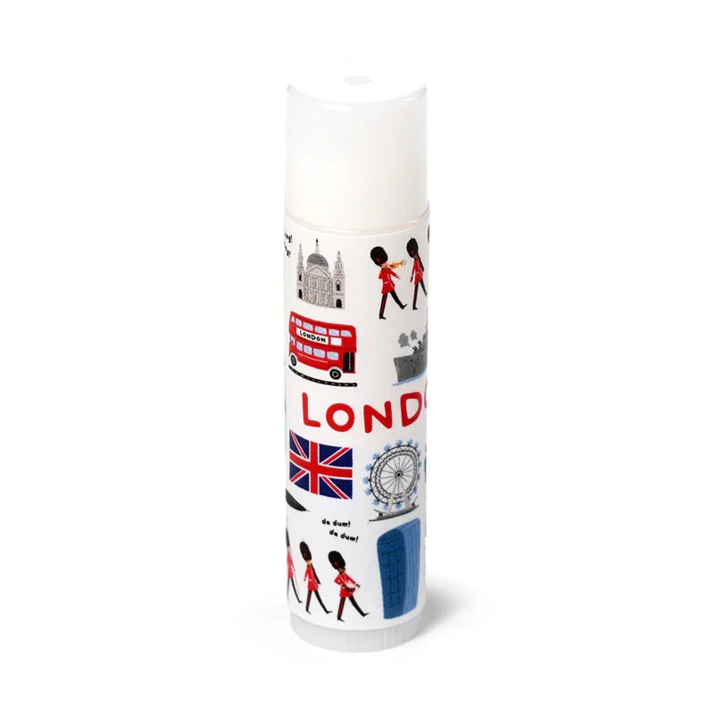 White lip balm stick standing upright, featuring colourful illustrations of London landmarks including a red double-decker bus, Union Jack flag, London Eye, and Royal Guards.