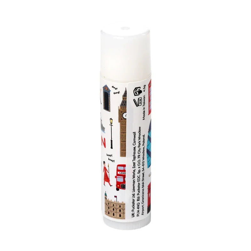 Angled view of a white lip balm stick with a clear cap, featuring London-themed illustrations including Big Ben, a red double-decker bus, and a Beefeater.