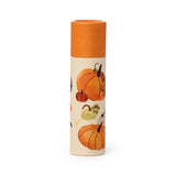 A cylindrical paper stick lip balm standing upright, with an orange cap and a cream tube featuring illustrations of various orange, green, and cream-coloured pumpkins.