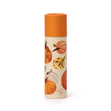 Paper stick lip balm with an orange cap and cream-coloured tube, shown from an angled view showcasing its autumnal pattern of various orange, white, and green pumpkins and gourds, with small mushrooms towards the base.