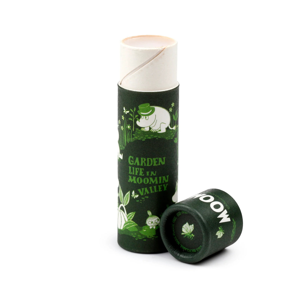 Angled product shot of a dark green paper stick lip balm. It features a white and light green Moomin Garden Life illustration with Garden Life in Moomin Valley text. The detached lid is beside it, showing 100% Plastic Free and 100% Recyclable text.