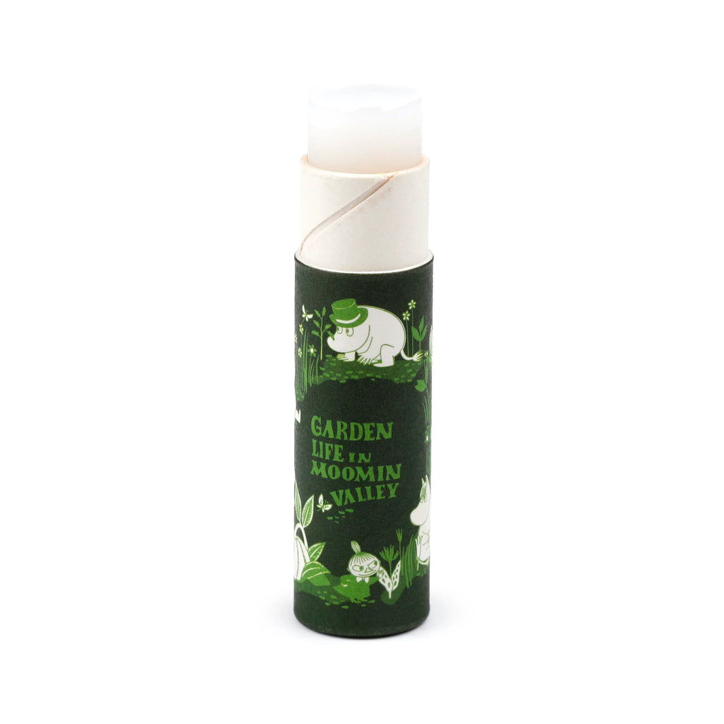 Front view of a dark green paper stick lip balm featuring a Moomin garden life illustration and 'Garden Life in Moomin Valley' text, with the white lip balm stick extended.