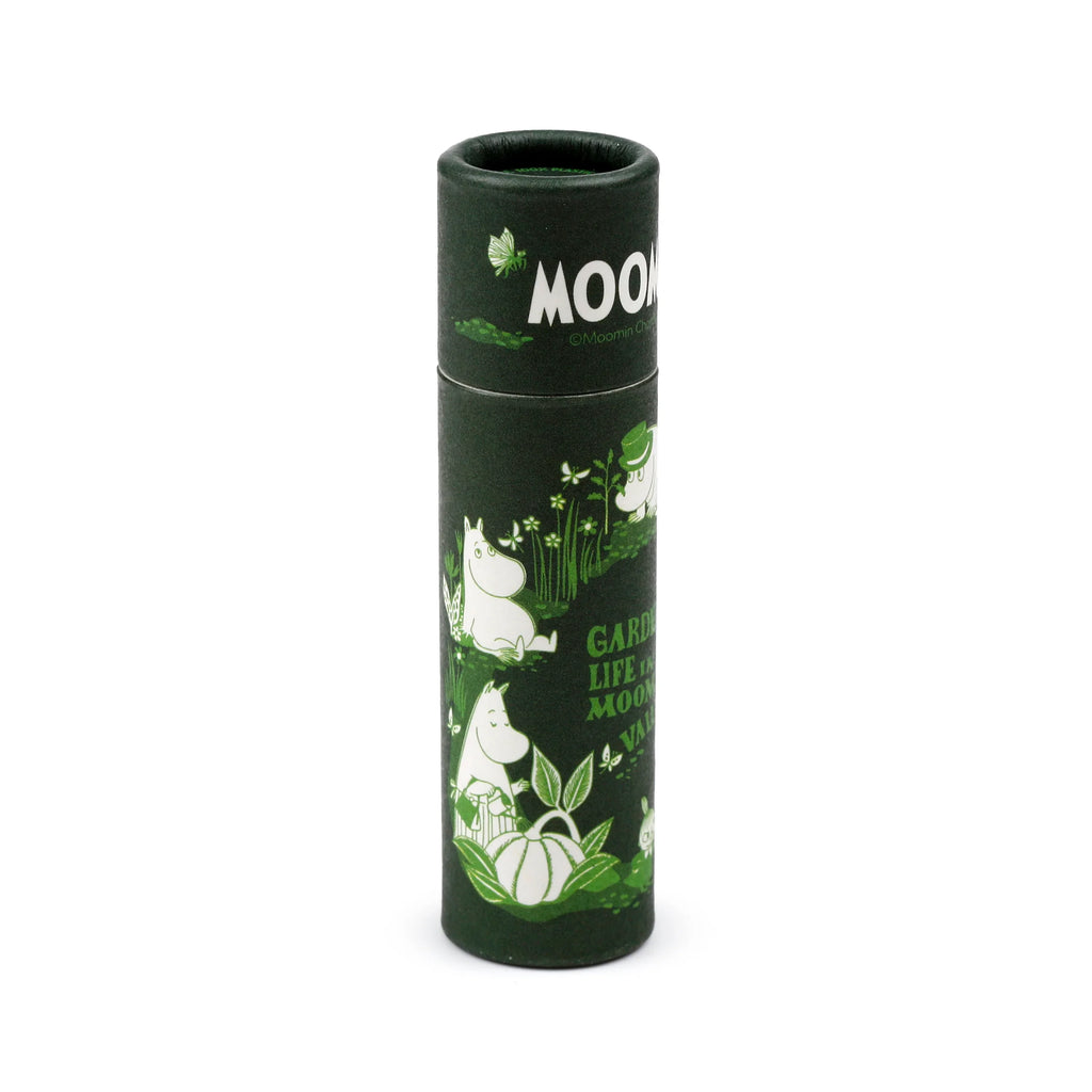 Angled view of a dark green paper stick lip balm tube, featuring white and light green illustrations of Moomin characters, garden foliage, and butterflies, with partial visible text 'MOO' and 'GARDEN LIFE'.