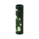 Angled view of a dark green cylindrical paper stick lip balm, decorated with white and light green illustrations of Moomin characters and garden foliage.