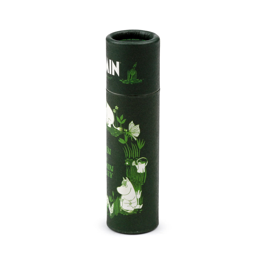Angled view of a dark green cylindrical paper stick lip balm, decorated with white and light green illustrations of Moomin characters and garden foliage.