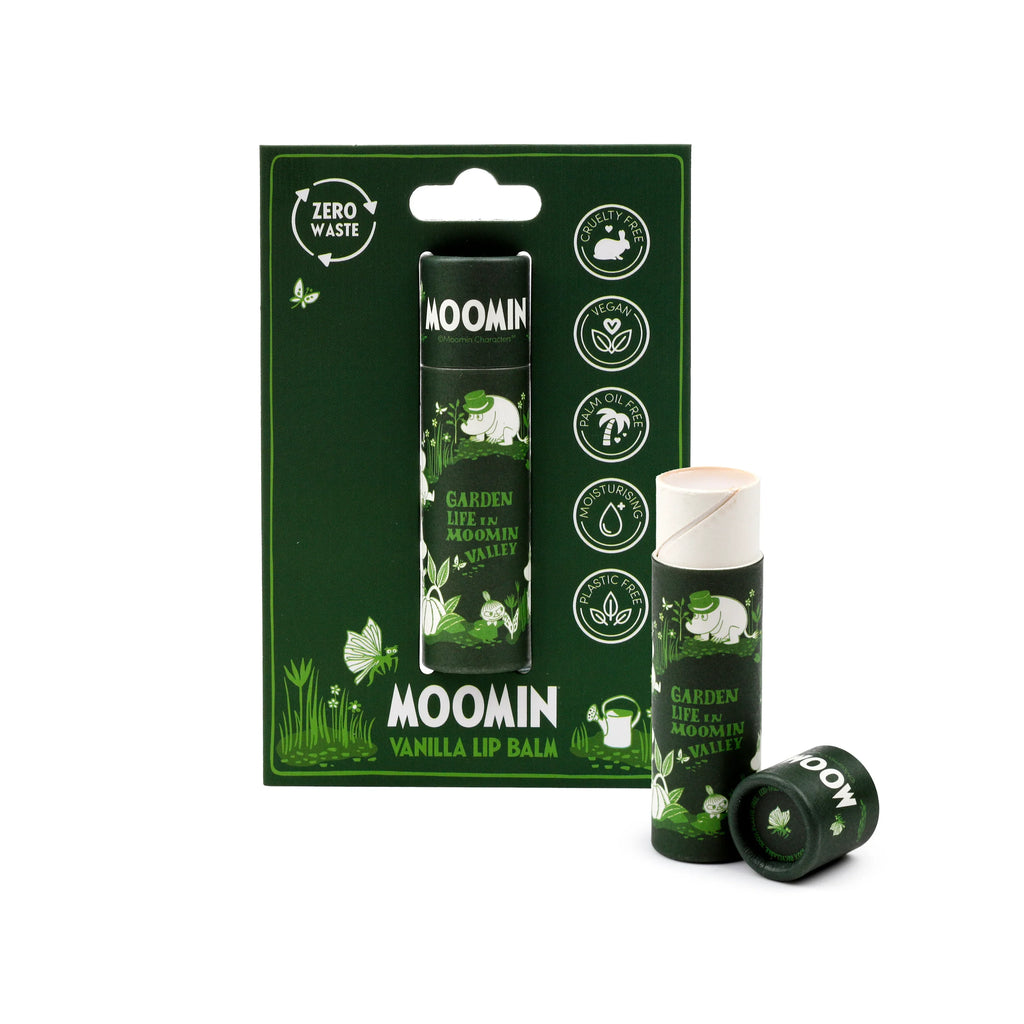Angled product shot of a Moomin Garden Life paper stick lip balm. A dark green retail card package, featuring Moomin characters amidst garden foliage, holds one 'Vanilla Lip Balm'. Nearby, a second paper stick lip balm stands partially open, revealing its white tip, and a third lies flat, its base showing '100% Recyclable' and 'Plastic Free' text. The packaging highlights 'Zero Waste', 'Cruelty Free', and 'Vegan' certifications.