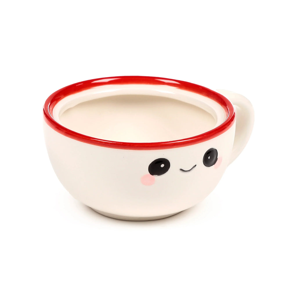 Angled view of a cream coloured ceramic mug with a red rim and a winking cartoon face, showing the handle and interior.