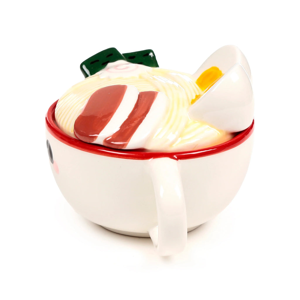 Angled view of a white ceramic lidded mug, designed as 'Nori the Ramen Foodiemals', with a red rim and handle. The lid features sculpted ramen noodles with green seaweed, a pink swirl narutomaki, reddish-brown slices, and a hard-boiled egg. A small face is on the mug body.