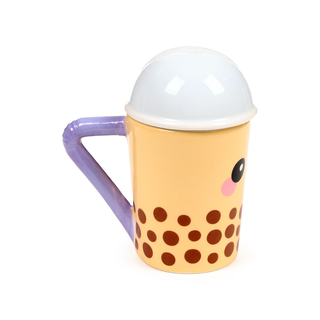 Angled view of a ceramic lidded mug shaped like a bubble tea cup. It has a light beige body with brown boba-like polka dots, a white domed lid, a purple handle, and a cartoon eye with a pink blush on the side.