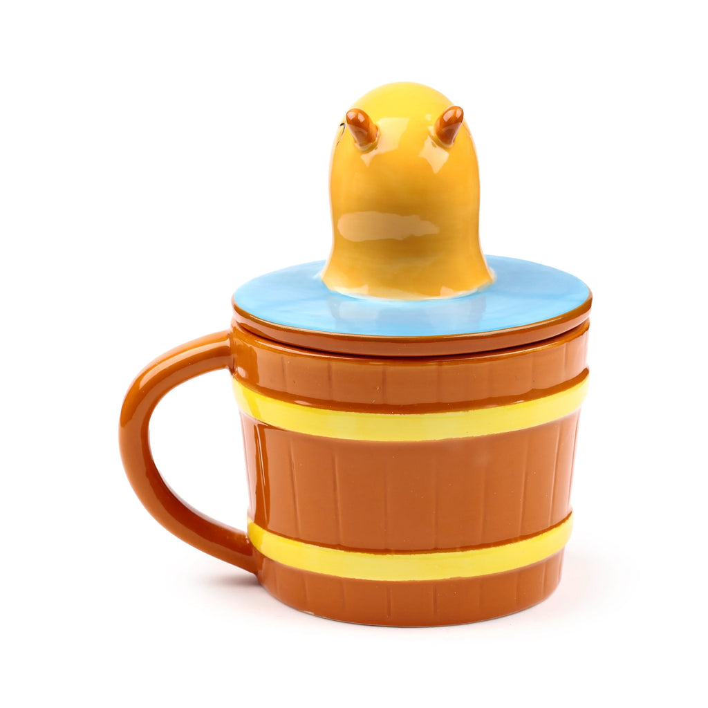 Angled side view of a ceramic lidded capybara mug, featuring a brown barrel-shaped body with yellow bands and a brown handle. A yellow capybara head emerges from the light blue lid.