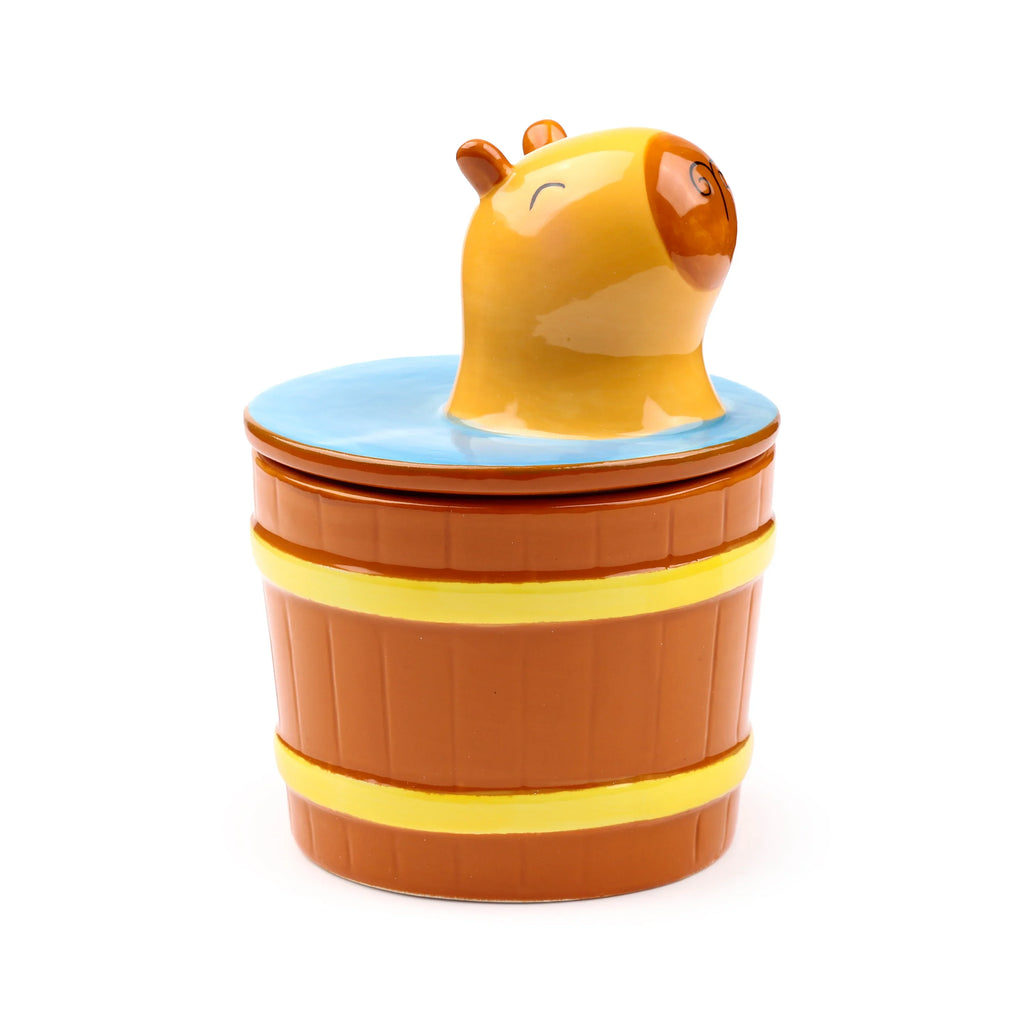 Angled view of a ceramic capybara lidded mug, shaped like a brown barrel with two yellow bands, topped with a lid featuring a capybara head emerging from blue water.