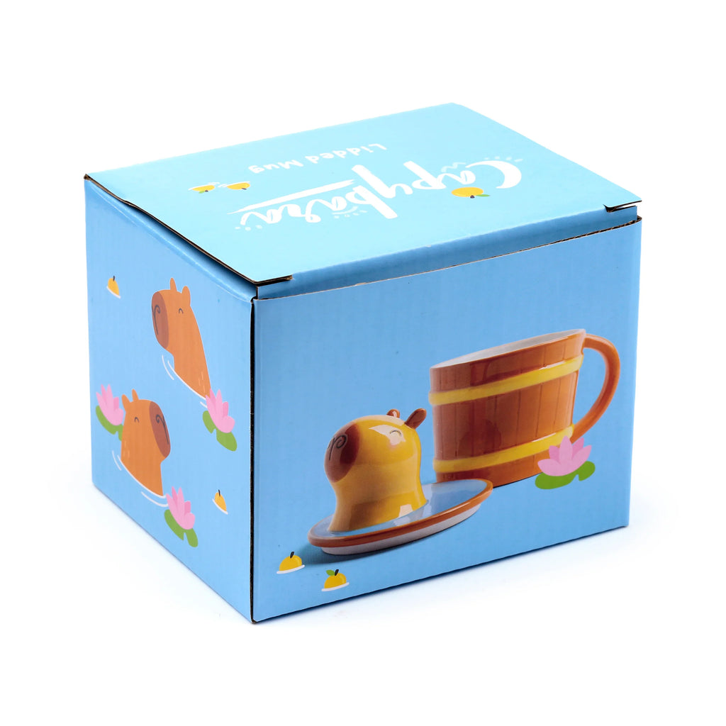 Angled view of a light blue packaging box for a Ceramic Capybara Lidded Mug, with cartoon capybara illustrations and an image of the brown lidded mug.