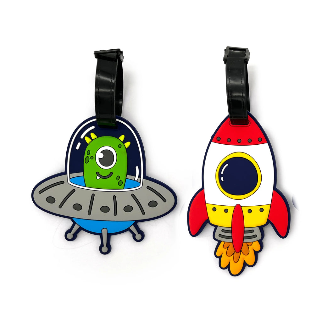 Angled overhead view of a set of two PVC luggage tags. One tag features a green alien in a grey flying saucer, and the other a red, white, and yellow rocket ship with flames, both with black attachment straps.