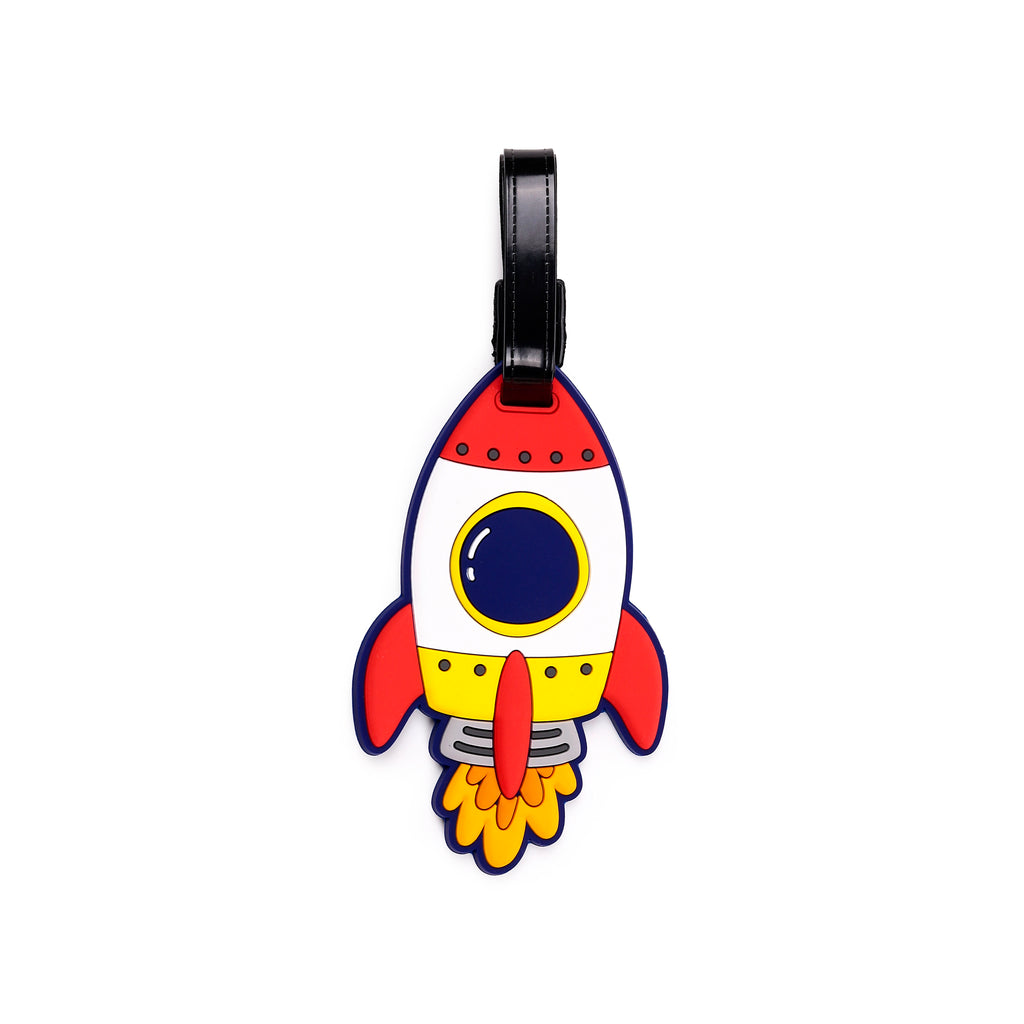 Front view of a colourful PVC luggage tag, shaped like a cartoon rocket. It features a red nose cone, a white body with a blue porthole outlined in yellow, yellow side fins, and stylised orange and red flame detailing at the base. A black strap is visible at the top.