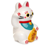 Three-quarter view of a white ceramic Maneki Neko lucky cat money box, with its paw raised, holding a yellow coin, and detailed with a red collar, teal bib, and red markings on its ears and paws.