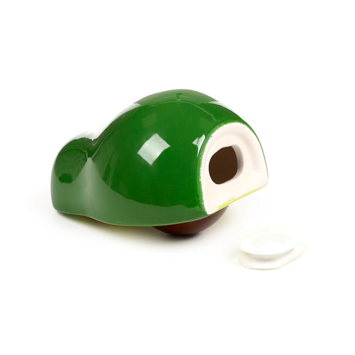 Green ceramic avocado money box lying on its side, showing its glossy finish, brown base, the money retrieval opening with a light-coloured rim, and a separate white rubber stopper.