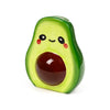 Ceramic avocado money box featuring a cheerful cartoon face with eyes, a smile, and pink blush, showing its large, glossy brown pit, from a front-angled view.