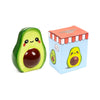 Front view of a glossy green ceramic avocado money box, with a happy face, pink cheeks, and a dark brown stone. It is displayed next to its light blue gift box, which features an illustration of the avocado character Pedro.