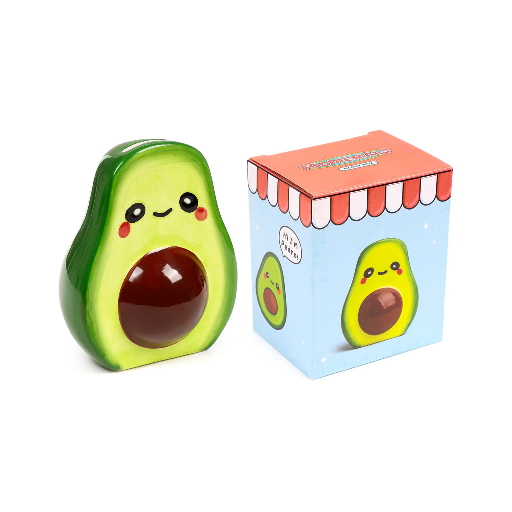 Front view of a glossy green ceramic avocado money box, with a happy face, pink cheeks, and a dark brown stone. It is displayed next to its light blue gift box, which features an illustration of the avocado character Pedro.