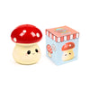 Angled view of a cute ceramic mushroom money box, featuring a red and white spotted cap and a cream base with a smiling face, displayed next to its illustrated packaging box.