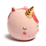 Angled view of a pink ceramic unicorn money box featuring a golden horn, dark pink mane, closed eyelashes, and rosy cheeks.