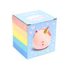 Angled view of ceramic money box packaging, featuring a light blue side with a pink unicorn head, golden horn, closed eyes, and rosy cheeks, surrounded by hearts and stars. The adjacent side displays vibrant rainbow stripes.