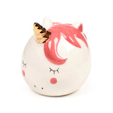 White ceramic unicorn money box, displaying its face with closed eyes, pink cheeks, a gold horn, and sculpted pink mane details.