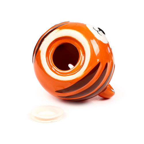 Angled view of an orange and dark brown ceramic tiger money box, with its circular coin slot visible and a cream-coloured stopper lying beside it.