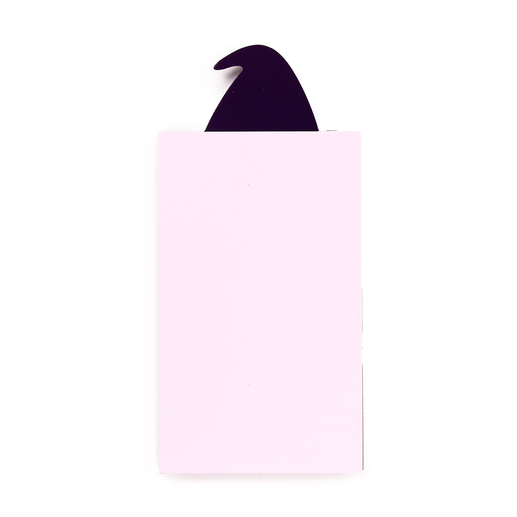 Overhead view of a light pink memo pad with a dark, pointed witch's hat shape emerging from the top.