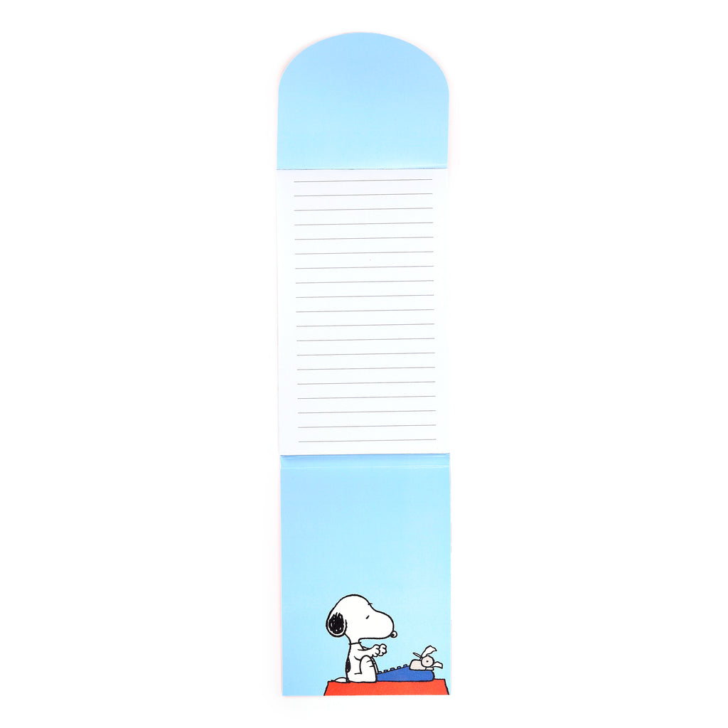 Overhead view of an unfolded light blue flip-open memo pad with lined paper, featuring an illustration of Snoopy typing on a blue typewriter with Woodstock perched on it.