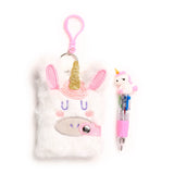 Front view of a white fluffy A7 notebook with a unicorn face design, featuring pink glitter ears, a golden glitter horn, purple embroidered eyes, and a pink clip, alongside a pink multi-colour pen topped with a small unicorn figure.