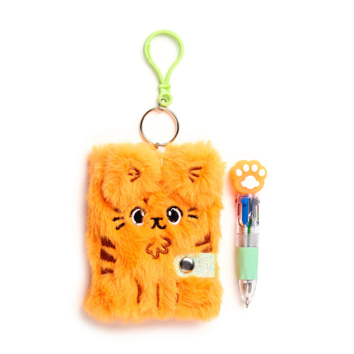 Top-down view of an orange plush cat notebook with an embroidered cat face and stripes, a glittery strap closure, and a light green carabiner clip, presented next to a light green multi-colour pen with an orange paw print top.