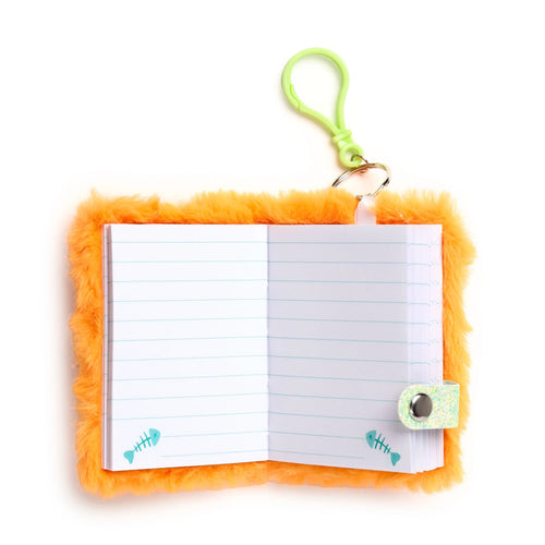 Overhead view of an open orange fluffy notebook with lined pages, teal fish skeleton motifs, a glittery closure tab, and a lime green carabiner clip.
