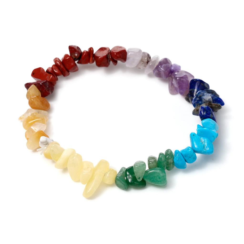 Overhead shot of a colorful gemstone bracelet made of natural chakra chip stones, arranged in a rainbow gradient on a white background.