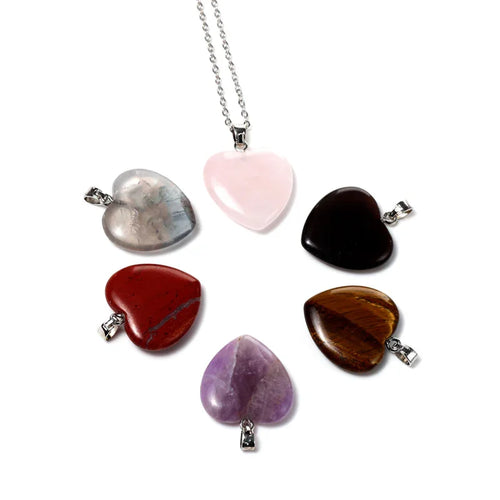 Overhead view of six interchangeable heart-shaped gemstone pendants in various colours, with one pink pendant attached to a silver-coloured chain.