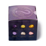 A purple Gemstone Mystery Box, shown from an elevated front view, features illustrations of amethyst, pyrite, cirtine, geode quartz, clear quartz, and rose quartz on its front panel. The top flap displays a question mark and the text 'Which crystals will choose you?'.