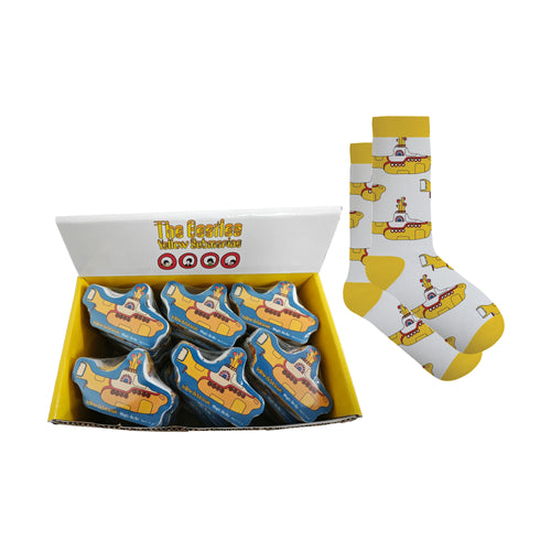 Angled view of a yellow retail display box containing multiple 'The Beatles Yellow Submarine' compressed magic socks in submarine-shaped packaging, shown next to an uncompressed pair of white socks with a yellow submarine pattern.