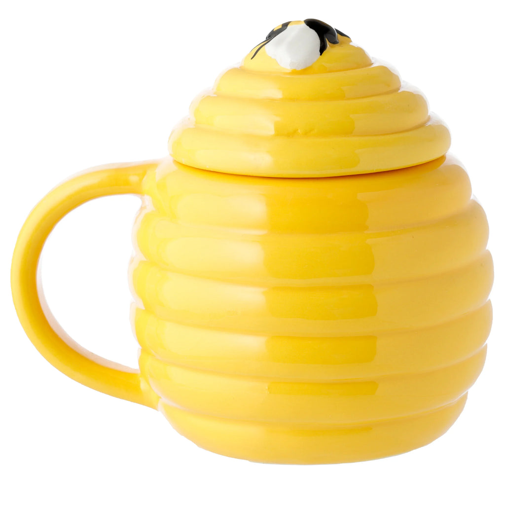 Side view of a bright yellow ceramic beehive mug with prominent horizontal ridges, featuring a matching lid topped with a small black and white bee decoration.