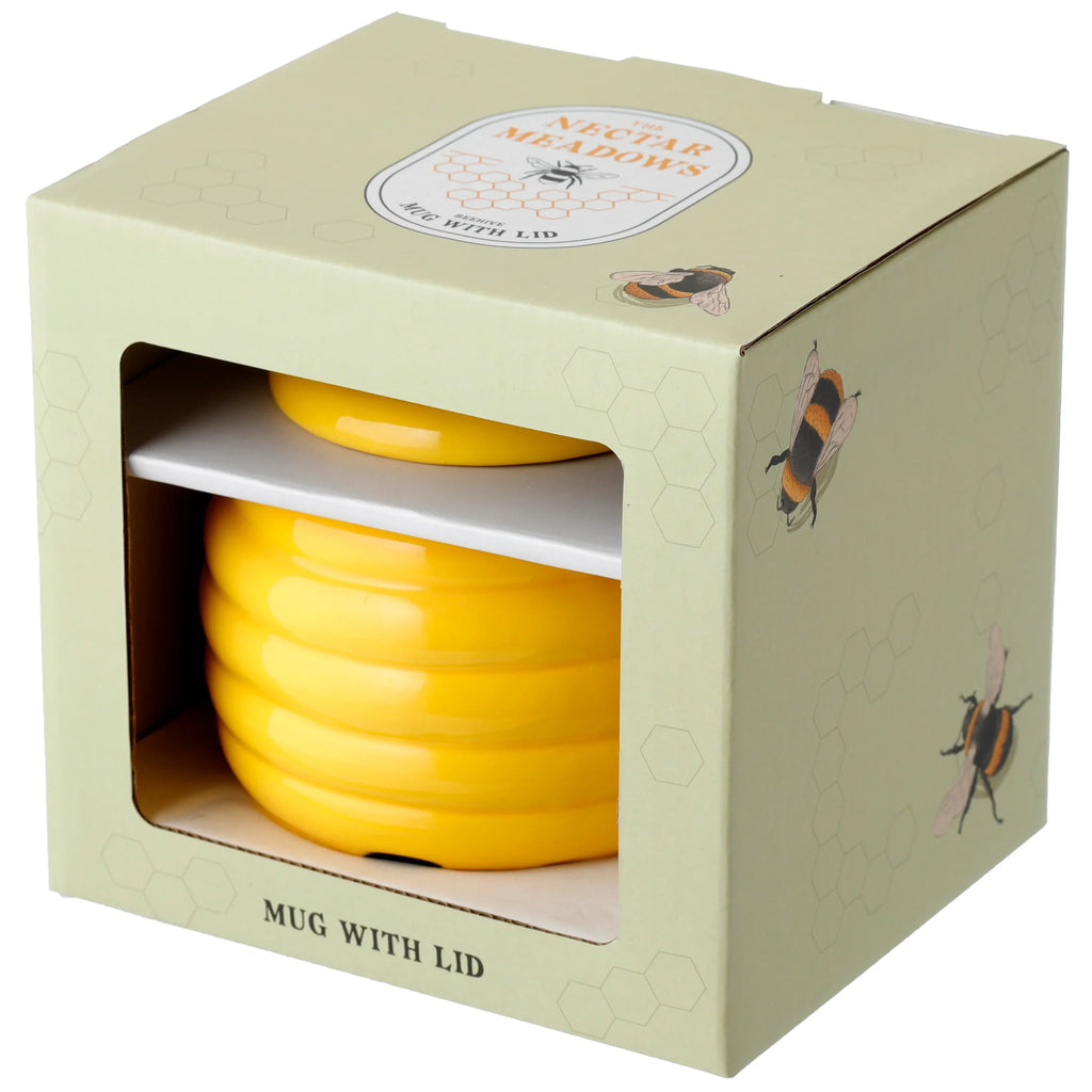 Angled view of a yellow ceramic beehive mug with lid, in its light green packaging box. The box shows bees, honeycomb patterns, and 'The Nectar Meadows' label.