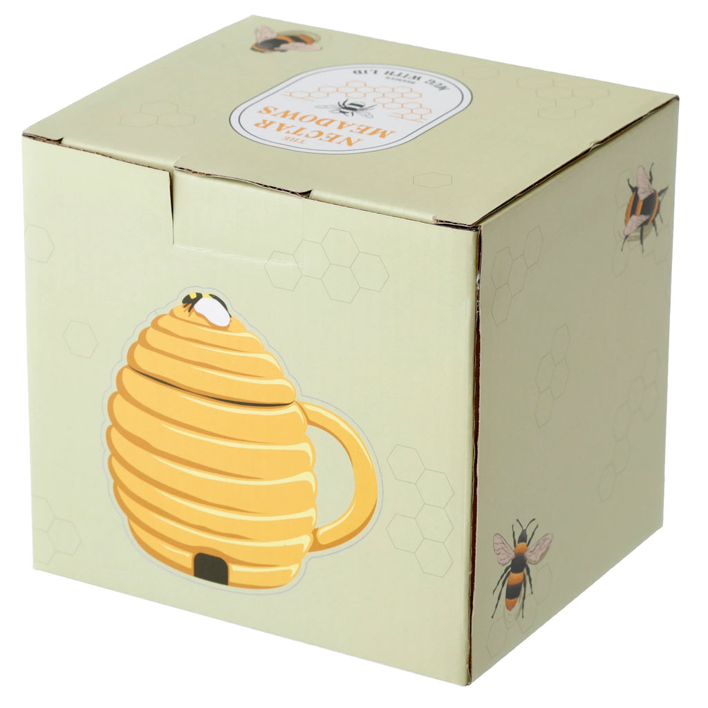Angled view of light green product packaging for a beehive shaped mug. The box displays an illustration of a yellow beehive mug with a bee on its lid, further bee graphics, and honeycomb patterns. Text on the box top reads 'The Nectar Meadows' and 'Mug with Lid'.
