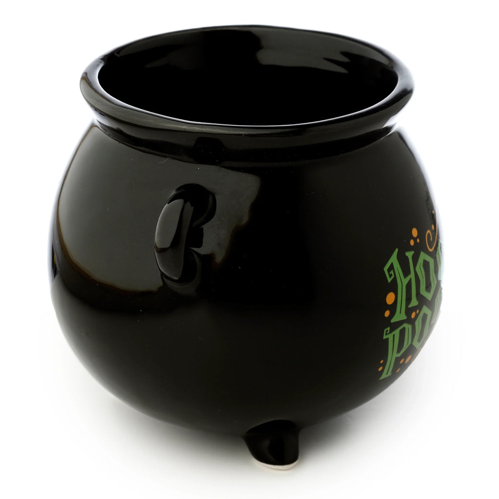 Angled view of a black ceramic cauldron-shaped mug, featuring a handle, three small feet, and partially visible green and orange 'Hocus Pocus' text on its side.