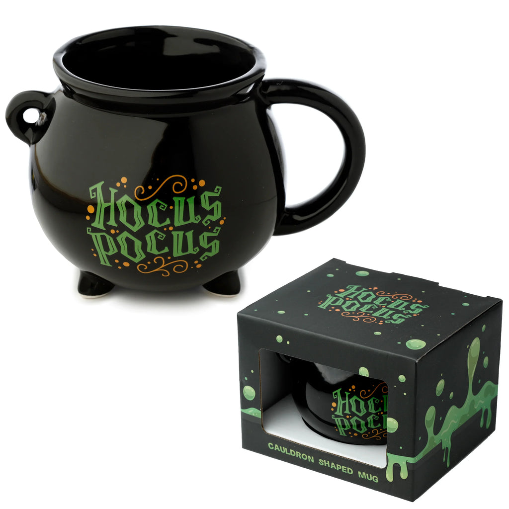 Angled view of a black ceramic cauldron-shaped mug, featuring green and orange 'Hocus Pocus' text and three feet, displayed next to its matching black retail box.