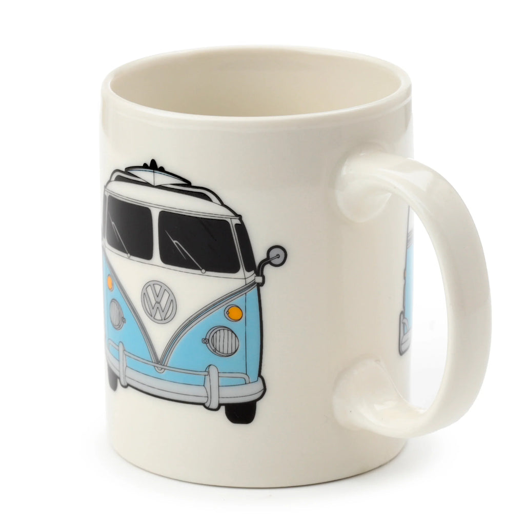 Angled view of a cream porcelain mug featuring a graphic of a light blue and white Volkswagen T1 Camper Bus with a surfboard on the roof.