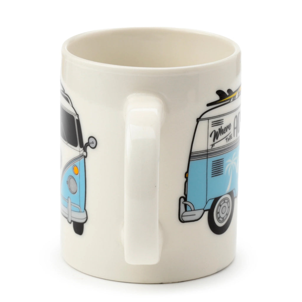 Angled view of a creamy white porcelain mug, featuring a continuous wraparound illustration of a blue and white camper bus. One side shows the front of the bus with a headlight, while the other side depicts the rear with a surfboard on the roof and a palm tree.