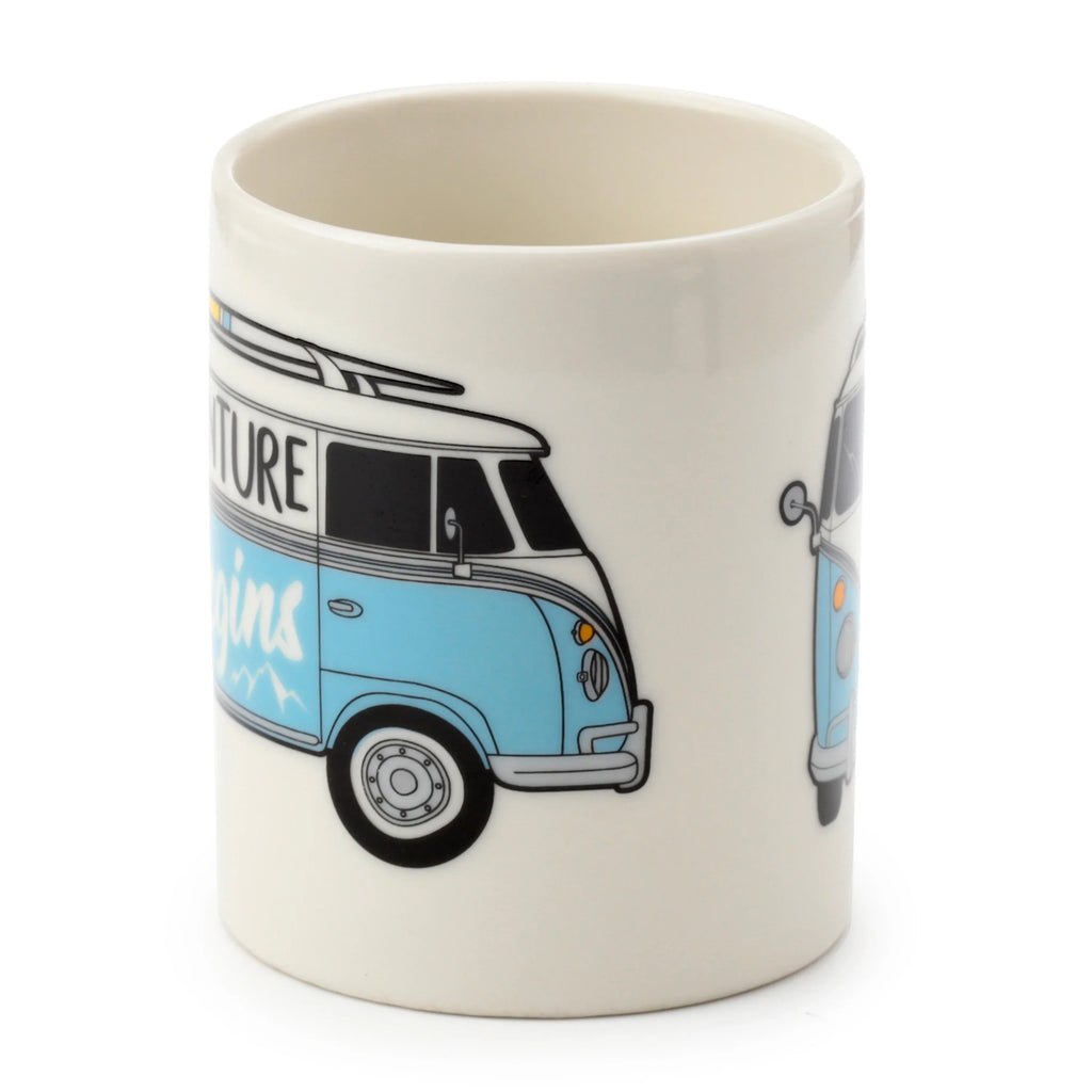 Angled view of a porcelain mug featuring a light blue and white VW T1 Camper Bus with surfboards on the roof and 'ADVENTURE begins' text.