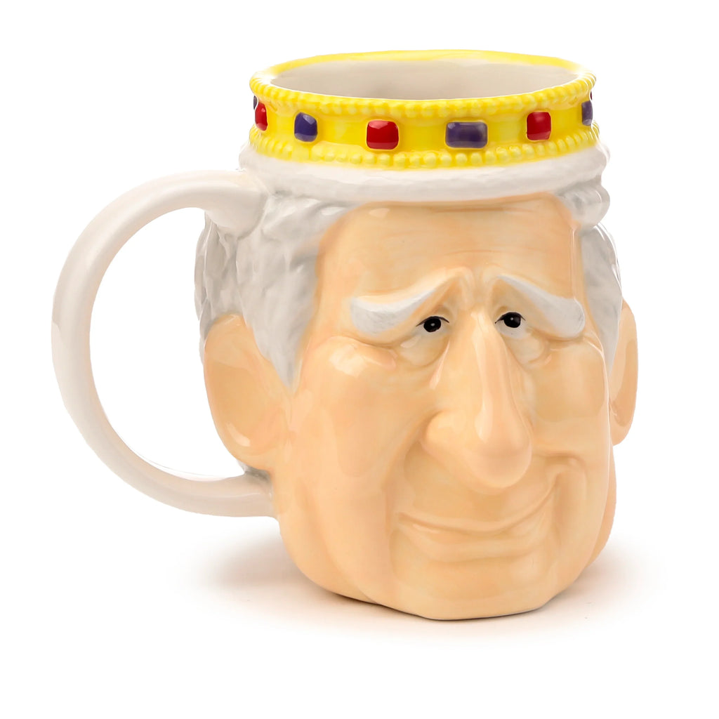 Front view of a ceramic King Charles III shaped head mug, featuring white hair, light skin tone, a yellow crown with red and purple jewels, and a cream-coloured handle.
