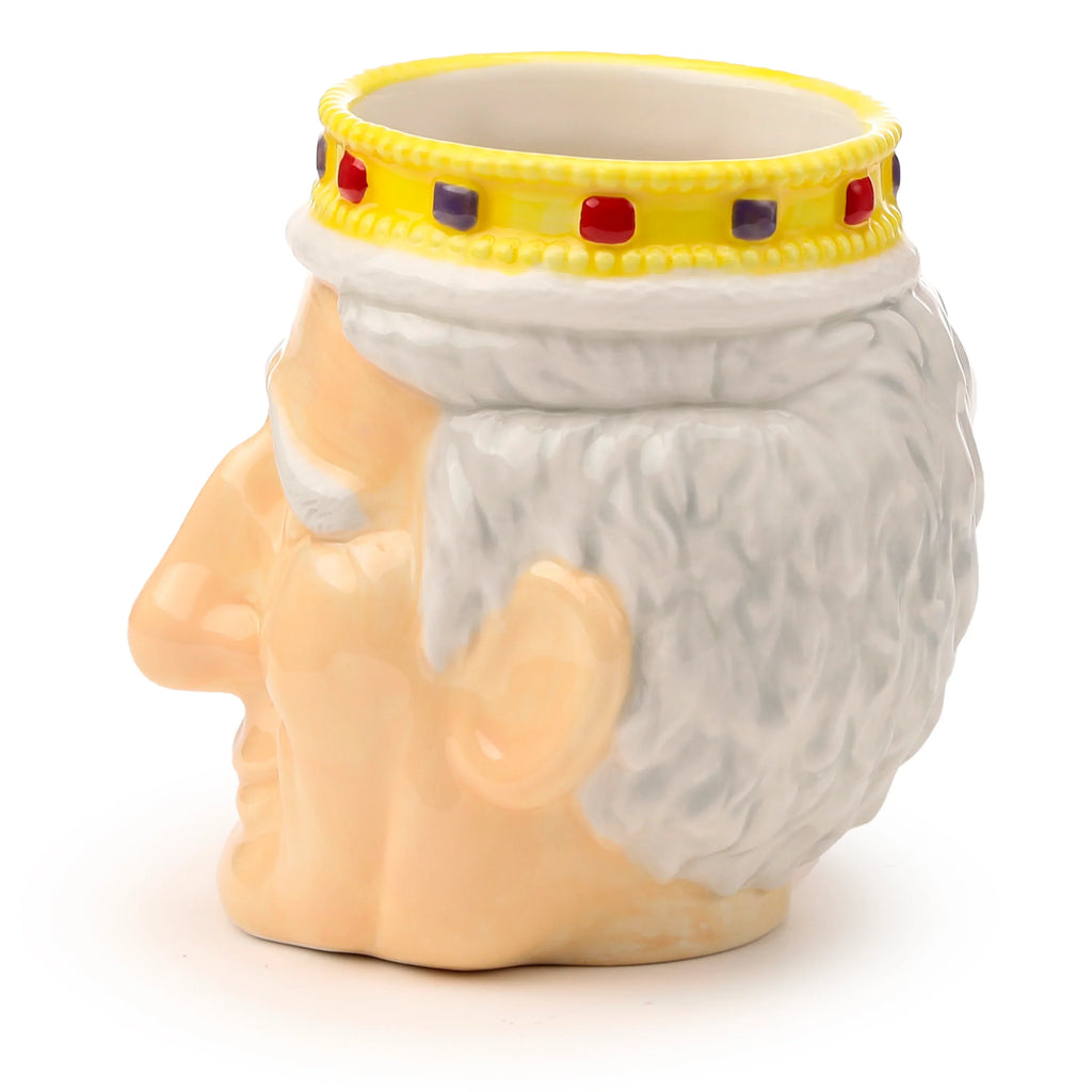Profile view of a ceramic King Charles III shaped head mug, featuring a yellow crown with red and purple jewels, white textured hair, and a peach skin tone.