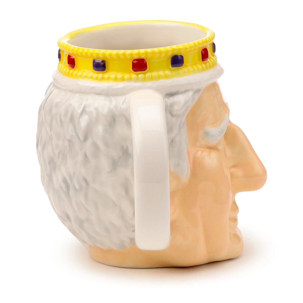 Side view of a ceramic King Charles III shaped head mug, displaying a flesh-toned profile, textured white hair, and a yellow crown adorned with red and purple jewels around the rim. The white handle is visible at the back.