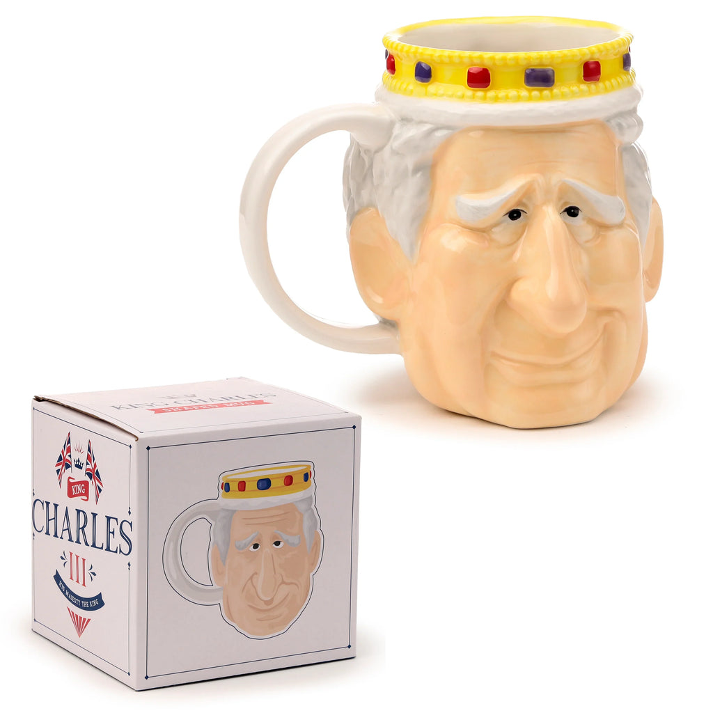 Angled view of a King Charles III ceramic shaped head mug, depicting his face and a yellow crown with red and blue details, positioned beside its white commemorative packaging box on a white background.